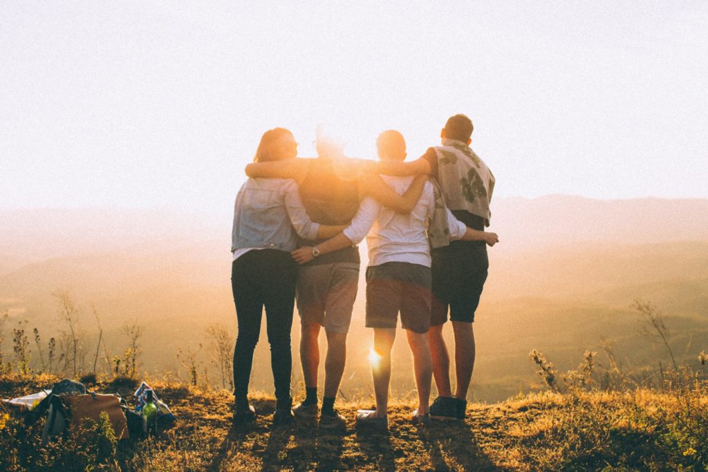 four people with arms around each other looking at sunset